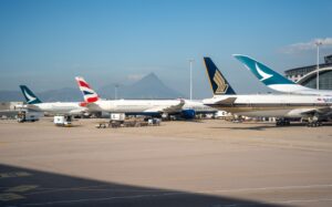 Multiple commercial airplanes parked at an airport terminal with a mountain view in the background.